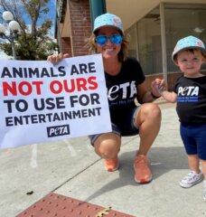 child and her mom on the sidewalk at a PETA protest holding signs that say "Animals are not ours to use for entertainment"