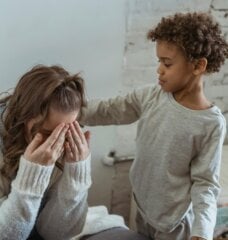 son is comforting his mom by touching her back while she cries.