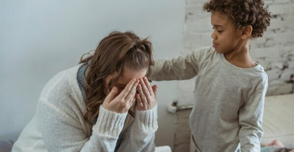 son is comforting his mom by touching her back while she cries.